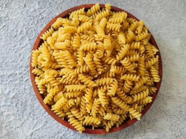 Gri desenli arka planda ahşap bir tabakta pişmemiş spiral makarna. Seçici odak resmi