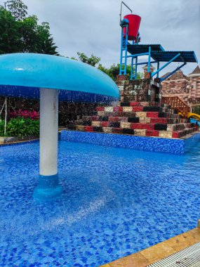 Yüzme havuzu, su kaydırağı, mantar suyu damlaları ve çocuklar için su kovası çöplüğü olan bir su parkı.