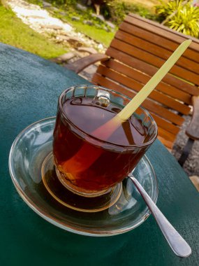 Enjoying a glass cup of hot aromatic tea (with lemon grass) in the backyard, bokeh background, selective focus image