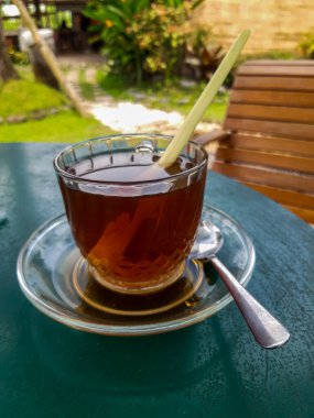 Enjoying a glass cup of hot aromatic tea (with lemon grass) in the backyard, bokeh background, selective focus image