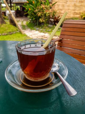 Enjoying a glass cup of hot aromatic tea (with lemon grass) in the backyard, bokeh background, selective focus image