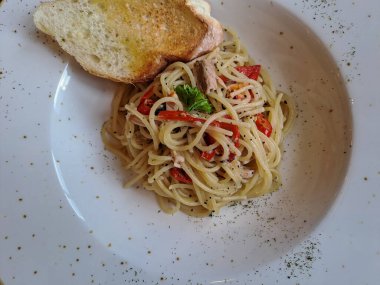 Aglio olio spaghetti topped with garlic bread. A traditional italian pasta served on the ceramic plate, ready to eat
