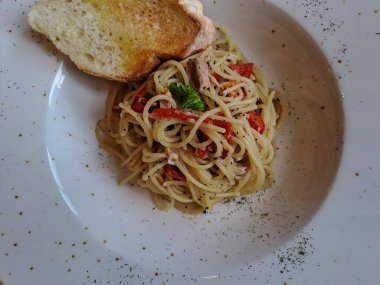 Aglio olio spaghetti topped with garlic bread. A traditional italian pasta served on the ceramic plate, ready to eat