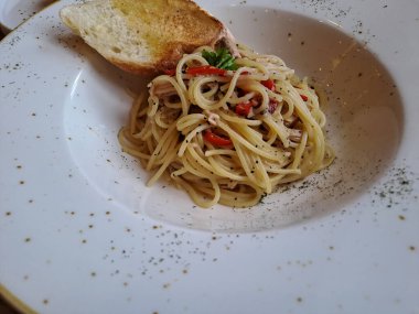 Aglio olio spaghetti topped with garlic bread. A traditional italian pasta served on the ceramic plate, ready to eat