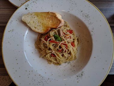 Aglio olio spaghetti topped with garlic bread. A traditional italian pasta served on the ceramic plate, ready to eat