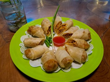 Lumpia, indonesian spring rolls, deep fried of wonton skin filled with stir fried of bamboo shoots, eggs and chicken or shrimp. Served in melamine plate on wooden table. Selective focus