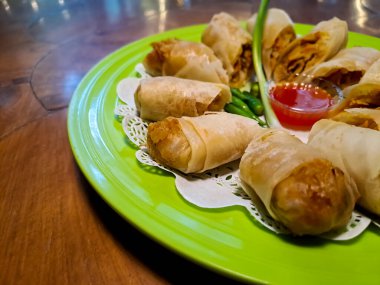 Lumpia, indonesian spring rolls, deep fried of wonton skin filled with stir fried of bamboo shoots, eggs and chicken or shrimp. Served in melamine plate on wooden table. Selective focus