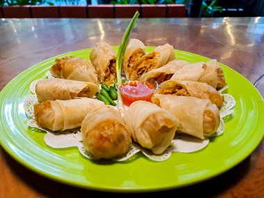 Lumpia, indonesian spring rolls, deep fried of wonton skin filled with stir fried of bamboo shoots, eggs and chicken or shrimp. Served in melamine plate on wooden table. Selective focus