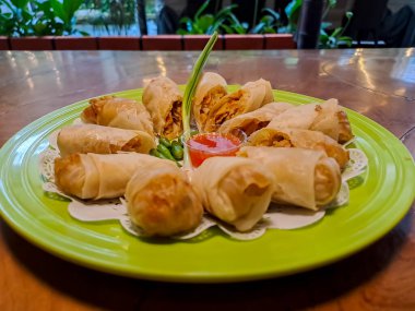 Lumpia, indonesian spring rolls, deep fried of wonton skin filled with stir fried of bamboo shoots, eggs and chicken or shrimp. Served in melamine plate on wooden table. Selective focus