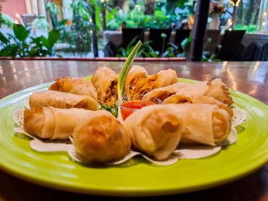Lumpia, indonesian spring rolls, deep fried of wonton skin filled with stir fried of bamboo shoots, eggs and chicken or shrimp. Served in melamine plate on wooden table. Selective focus