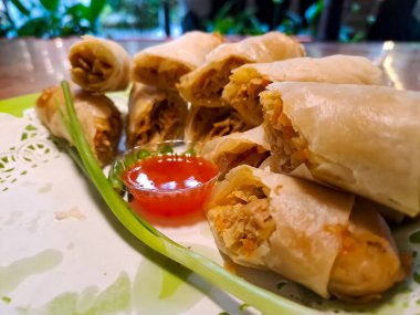 Lumpia, indonesian spring rolls, deep fried of wonton skin filled with stir fried of bamboo shoots, eggs and chicken or shrimp. Served in melamine plate on wooden table. Selective focus