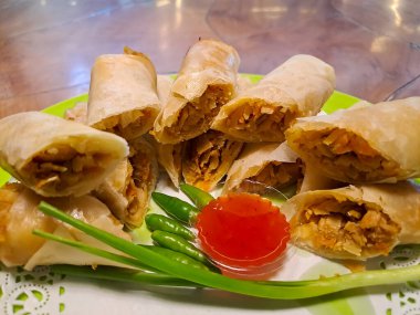 Lumpia, indonesian spring rolls, deep fried of wonton skin filled with stir fried of bamboo shoots, eggs and chicken or shrimp. Served in melamine plate on wooden table. Selective focus