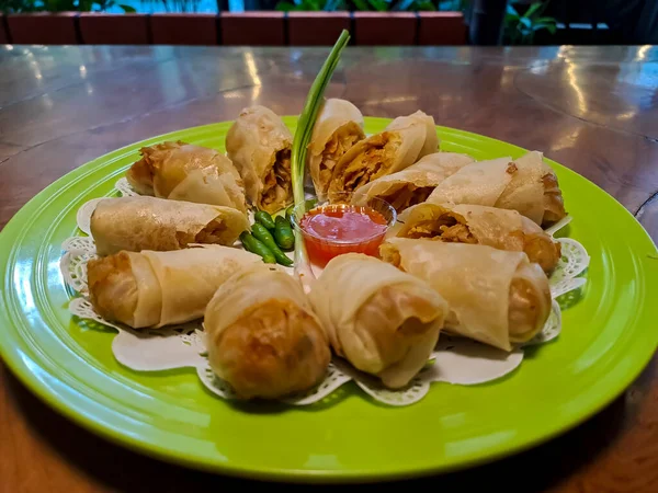 Lumpia, indonesian spring rolls, deep fried of wonton skin filled with stir fried of bamboo shoots, eggs and chicken or shrimp. Served in melamine plate on wooden table. Selective focus