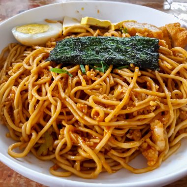 Stir fried noodles with chicken egg, tofu and seaweed topping, served on white bowl with chopsticks. Asian style food. Close up, selective focus