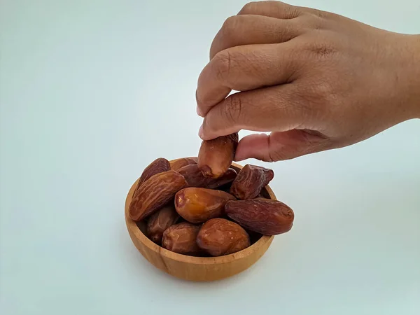 Human hand take a dates fruit from a wooden bowl, isolated on white background. Concept of break fasting in ramadan month, negative space, selective focus