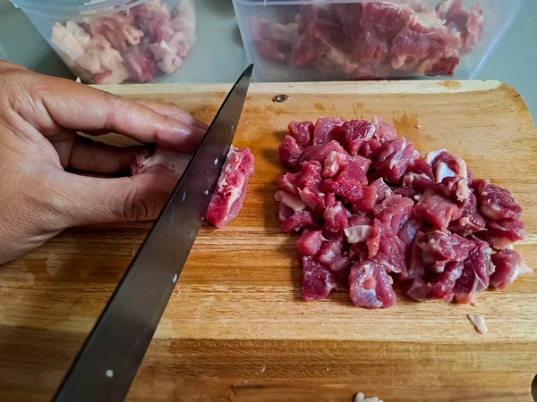 Food preparation, human hand slicing raw meat on a wooden cutting board. Fresh beef cutting with knife before cook. Selective focus