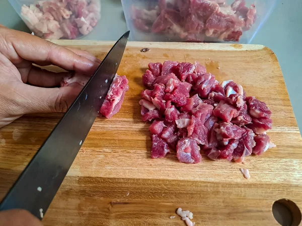 Food preparation, human hand slicing raw meat on a wooden cutting board. Fresh beef cutting with knife before cook. Selective focus