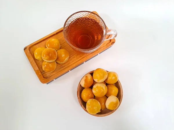 stock image Indonesian tart cookie with pineapple jam filling or Nastar served on wooden tray with a cup of tea isolated on white background. Tea or snack time concept