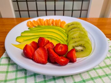 Meyveleri beyaz tabakta dilimle. Taze avokado, çilek, portakal ve kivi sağlıklı atıştırmalıklar için servis edilir. Diyet menüsü için uygun ya da ramazanda oruç tutmak