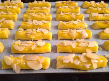 Kurabiye hamurunun dikdörtgen şeklinde şekli ve üzerine fırınlanmaya hazır bir tepsi konmuş badem dilimleri.