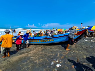 Depok Beach, Yogyakarta, Endonezya 'da 23 Nisan 2023' te denize açıldıktan sonra tekneyi kıyıdan çekmek için birlikte çalışan balıkçı..