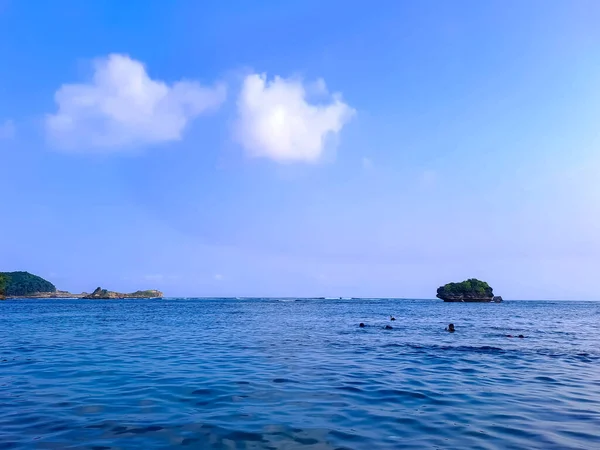 stock image Blue sea and sky with some tourists are swimming and rocks in the background