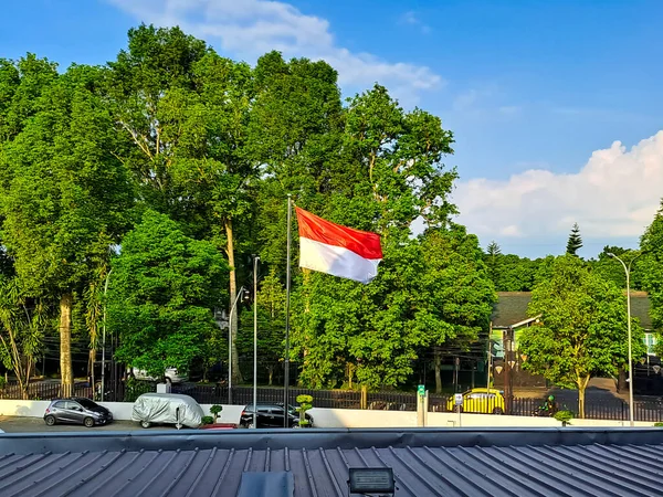 stock image View of Indonesian flag fluttering with green trees and clear cloudy sky in the background