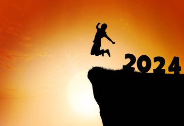 2024 'ten dağ sırasının tepesine sıçrayan bir insanın silueti. Mutlu yıllar ve Noel konsepti.