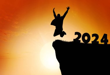 2024 'ten dağ sırasının tepesine sıçrayan bir insanın silueti. Mutlu yıllar ve Noel konsepti.