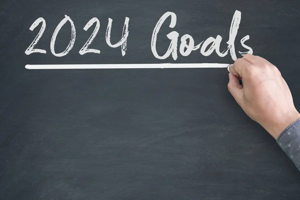 2024 Goals new year. A male hand writing new year goals on chalkboard.