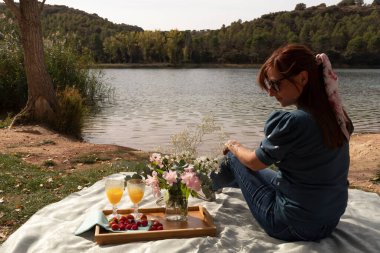 Kız gölün kıyısında piknik süslemeleri, çiçekleri, meyveleri ve meyve sularıyla