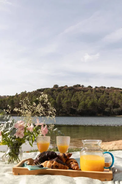 Göl kıyısında kruvasan ve çiçeklerle süslenmiş bir piknik.