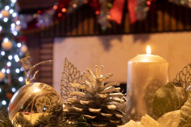 Noel süslemesi, içinde mum olan bir süs, arka planda bir ağaç ve şömine.