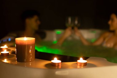 Jakuzide mum ışığında şarap içen çift.