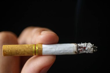 Sigaranın detaylarını gösteren iki parmağı olan birinin elinde tuttuğu sigaranın yakın görüntüsü. Siyah üzerine izole edilmiş.. 