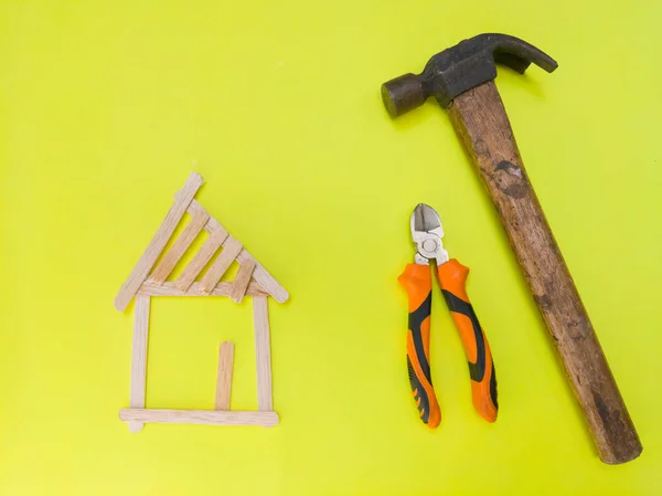 An illustration of a house renovation. Close up shot of a hammer, a pair of pliers, and some ice cream sticks. An illustration of under renovation.