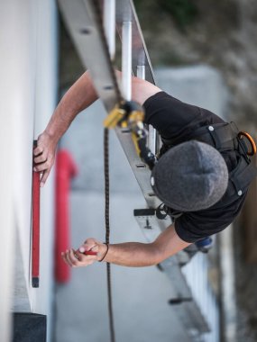 Ekibin bir elektrik mühendisi otonom fotovoltaik güneş paneli sisteminin elektrik kablolarını kuruyor. Bir ölçek üzerine kurulur ve konum ölçümleri ve matkap için bir metre ve bir kalem kullanır. Güvenliği için bir emniyet kemeri var.