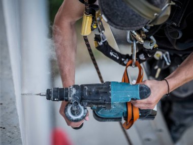 Ekibin bir elektrik mühendisi otonom fotovoltaik güneş paneli sisteminin elektrik kablolarını kuruyor. Bir ölçek üzerine kurulur ve konum ölçümleri ve matkap için bir metre ve bir kalem kullanır. Güvenliği için bir emniyet kemeri var.