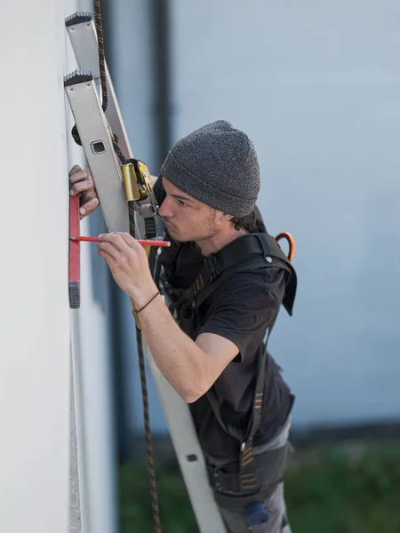 an electrical engineer of the team installs the electrical cables for the autonomous photovoltaic solar panel system. It is installed on a scale and uses a meter and a pencil for position measurements and a drill. For its safety it has a harness conn