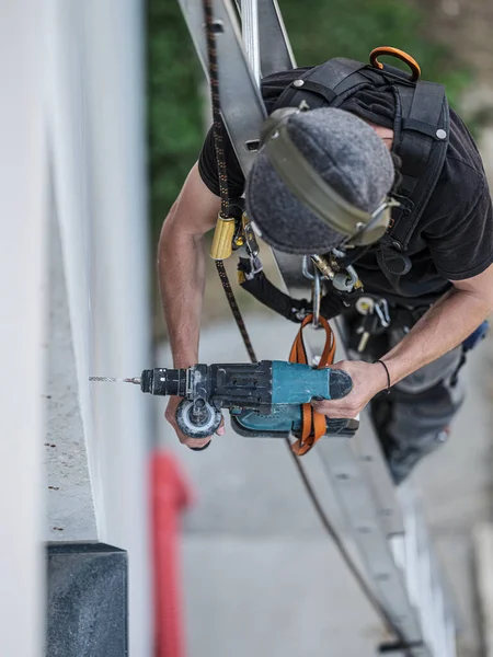 an electrical engineer of the team installs the electrical cables for the autonomous photovoltaic solar panel system. It is installed on a scale and uses a meter and a pencil for position measurements and a drill. For his safety he has a harness conn