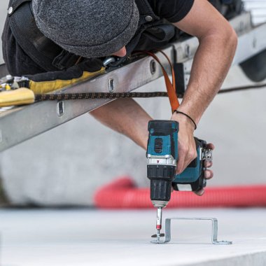 An electrical engineer of the team installs the electrical cables for the autonomous photovoltaic solar panel system. One of them is installed on a scale and use a drill to attach the chute that will support electrical cables from solar panels