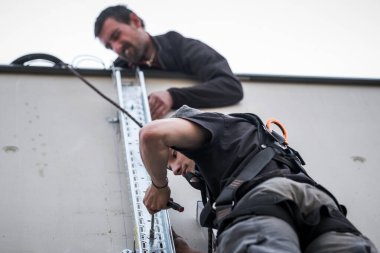 team of electrical engineers install the electrical cables for the autonomous photovoltaic solar panel system.One of them is installed on a scale and use a screwdriver to attach the chute that will support electrical cables from solar panels