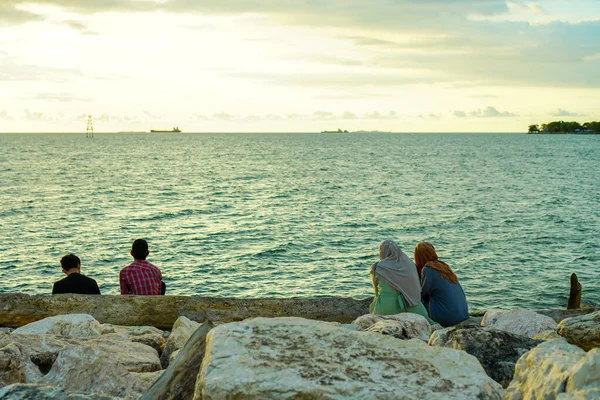 Friends sitting on a rock and looking at the waves. Women wear hijab