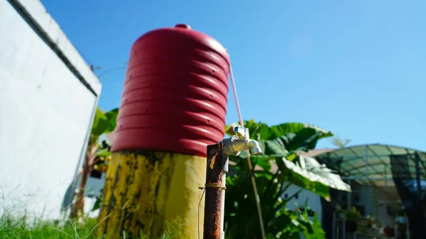 Water faucet with a hydroponic garden and green house in the background