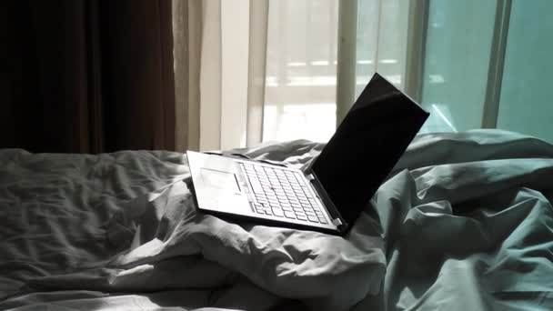 窓から美しい日光のストリーミングでベッドの上でスローモーションノートパソコンのショットを傾けます — ストック動画