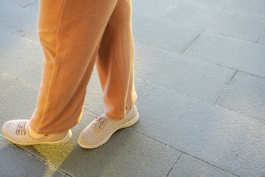 Fotokopi alanı kompozisyonu olan fayanslı bir zeminde duruyor. Uzun pantolon ve düz ayakkabı giyen bir kadın bacak mankeni.