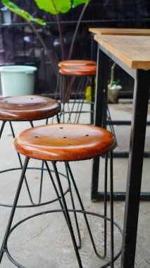 Gri beton zeminde sırtı olmayan ahşap ve metal tabureler. Tahta ve demirden yapılmış minimalist kafe sandalyeleri. Kenardan görülen seçmeli odak