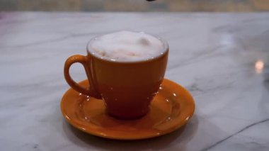 Portakallı kahve fincanında köpüklü bir cappuccino karıştıran Yavaş El Hareketi