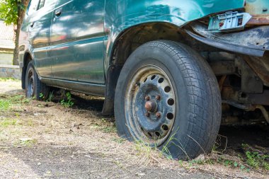İhmal edilmiş yeşil bir araba aşırı büyümüş bir arsada oturur ve güneş altında lastikleri patlak, ön parçaları eksik izler gösterir. Çevreleyen bitki örtüsü, olay yerinin çürümesine neden olur..