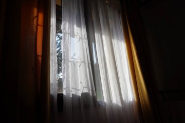 Parlak güneş ışığı, şeffaf perdelerden süzülerek odada yumuşak ve davetkar bir ortam yaratıyor. Doğal ışık ve kumaş dokularının birleşimi huzurlu ve rahat bir atmosfer yaratır.